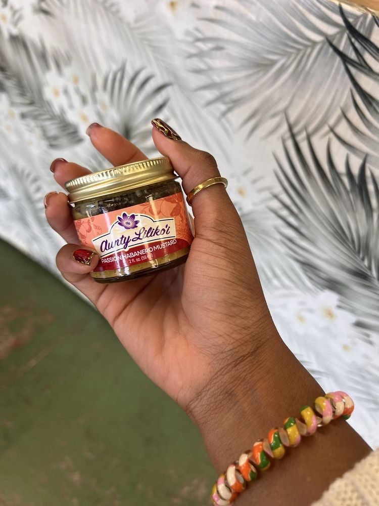 A hand holding a small jar of Aunty Lilikoʻi Passion Fruit Habanero Mustard