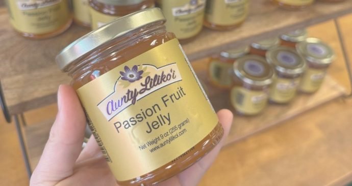 A hand holding a jar of Passion Fruit Jelly in front of the store shelves